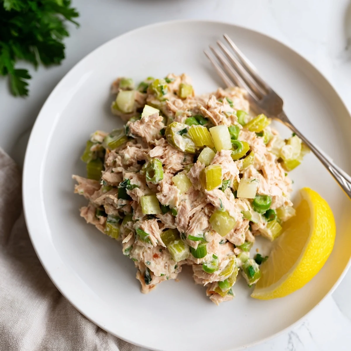 A close-up of Spicy Zesty Tuna Salad in a white bowl, showing the creamy texture and flecks of green scallions and fresh herbs.
