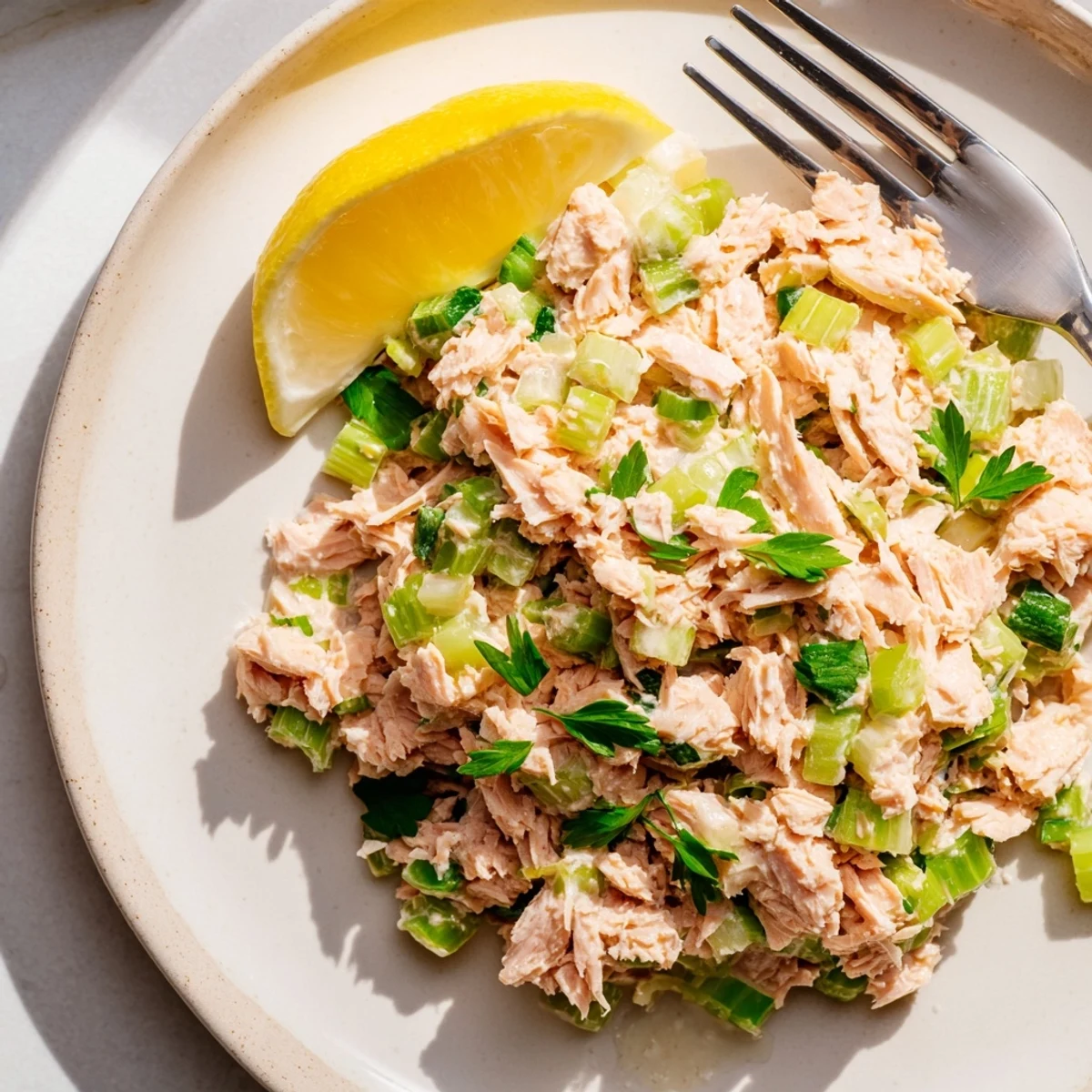 Vibrant plated Spicy Zesty Tuna Salad garnished with parsley and lemon, ready to serve with a fork nearby.