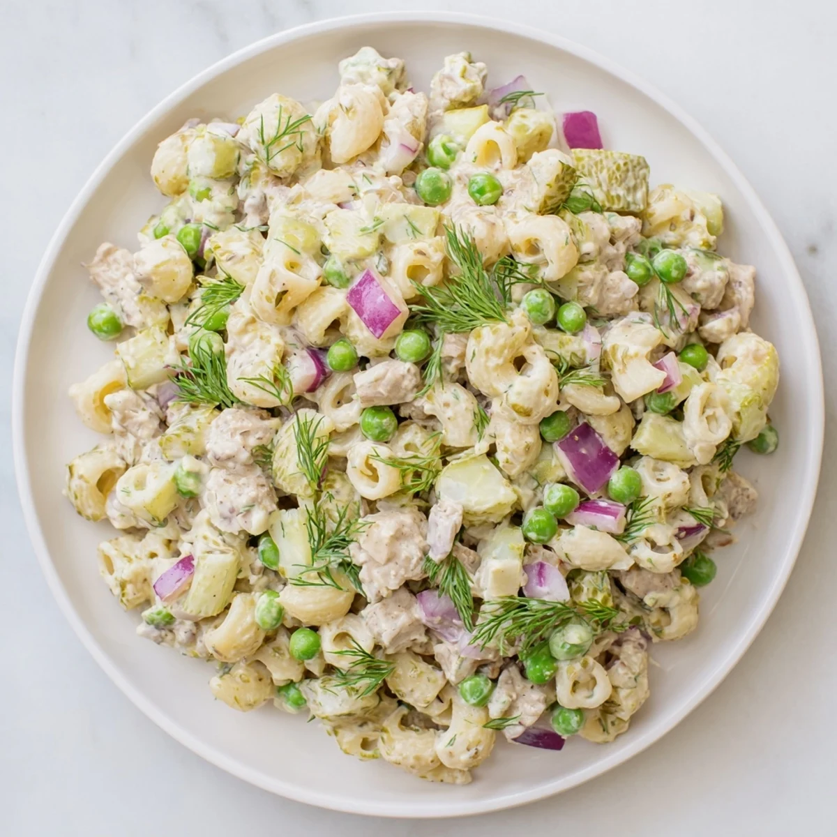 Creamy Dill Pickle Pasta Salad in a white bowl, featuring ditalini, peas, and diced pickles with a creamy dressing and fresh dill garnish.  