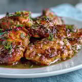 A close-up of tender Slow Cooker Honey Mustard Chicken coated in a glossy, savory sauce with garlic and herbs.
