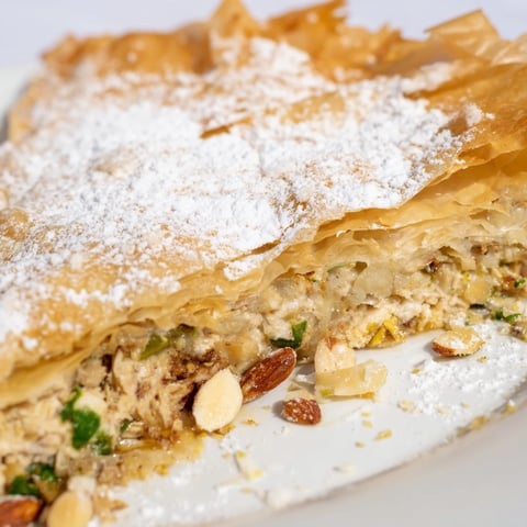 Golden-brown, flaky Moroccan Pastilla Pie, a savory meat pie dusted finely with sweet powdered sugar.