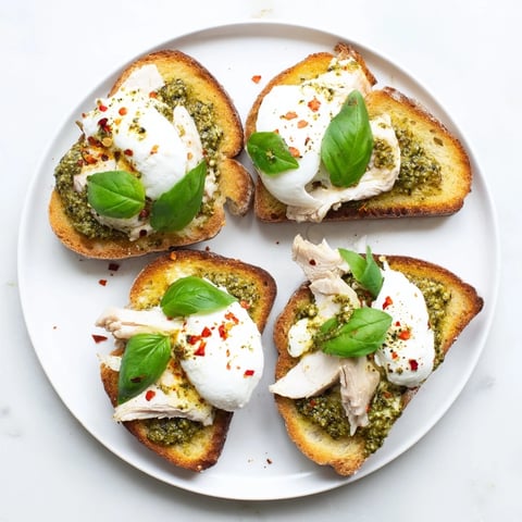 Golden, crusty sourdough toast topped with sliced pesto chicken and creamy burrata, garnished with fresh basil leaves for an Italian-inspired appetizer.