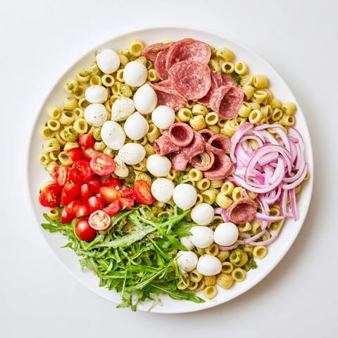 A vibrant bowl of Spring Antipasto Pasta Salad with ditalini, peppery arugula, and mozzarella pearls.
