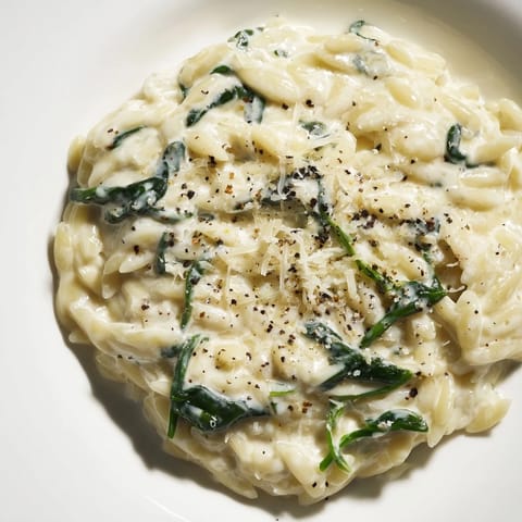 A close-up of Creamy Spinach Orzo reveals tender pasta, glistening with Parmesan, ready to serve and enjoy.