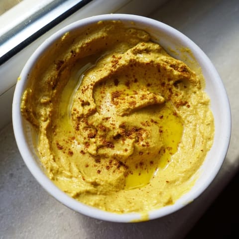 A bowl of homemade Chickpea Curry Paste, rich with turmeric and cumin, surrounded by pita chips and crunchy vegetable sticks for dipping.  