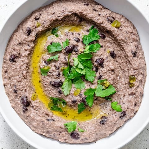 Spicy black bean dip served in a rustic bowl with blue corn tortilla chips for dipping.  