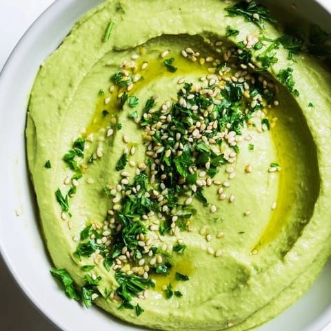 Edamame Hummus swirled in a rustic white bowl, garnished with a drizzle of olive oil and chopped parsley for a fresh appetizer.  