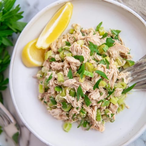 Spicy Zesty Tuna Salad in a rustic sandwich, layered with crisp lettuce and lemon wedges on a wooden cutting board.