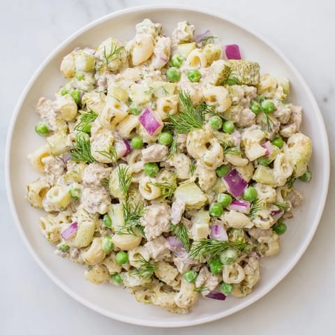Creamy Dill Pickle Pasta Salad in a white bowl, featuring ditalini, peas, and diced pickles with a creamy dressing and fresh dill garnish.  