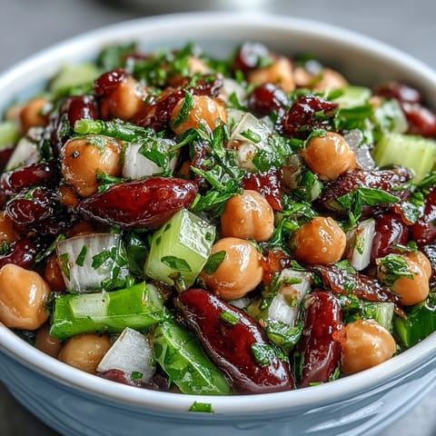 A vibrant bowl of Three-Bean Salad, featuring green beans, kidney beans, and chickpeas in a tangy apple cider vinaigrette with fresh parsley and crisp celery.