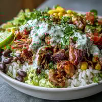 Golden-brown carnitas, fluffy rice, black beans, and sweet corn fill this vibrant Carnitas Burrito Bowl, topped with crisp lettuce, zesty salsa, and tangy lime crema.  