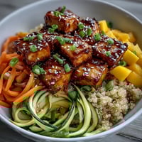 A vibrant Easy Teriyaki Quinoa Bowl with golden baked tofu, spiralized zucchini and carrots, sweet mango, and glossy teriyaki sauce.