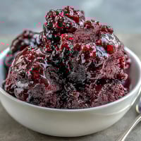 A scoop of vibrant Black Currant Sorbet in a glass dish, garnished with fresh berries for a refreshing vegan dessert.